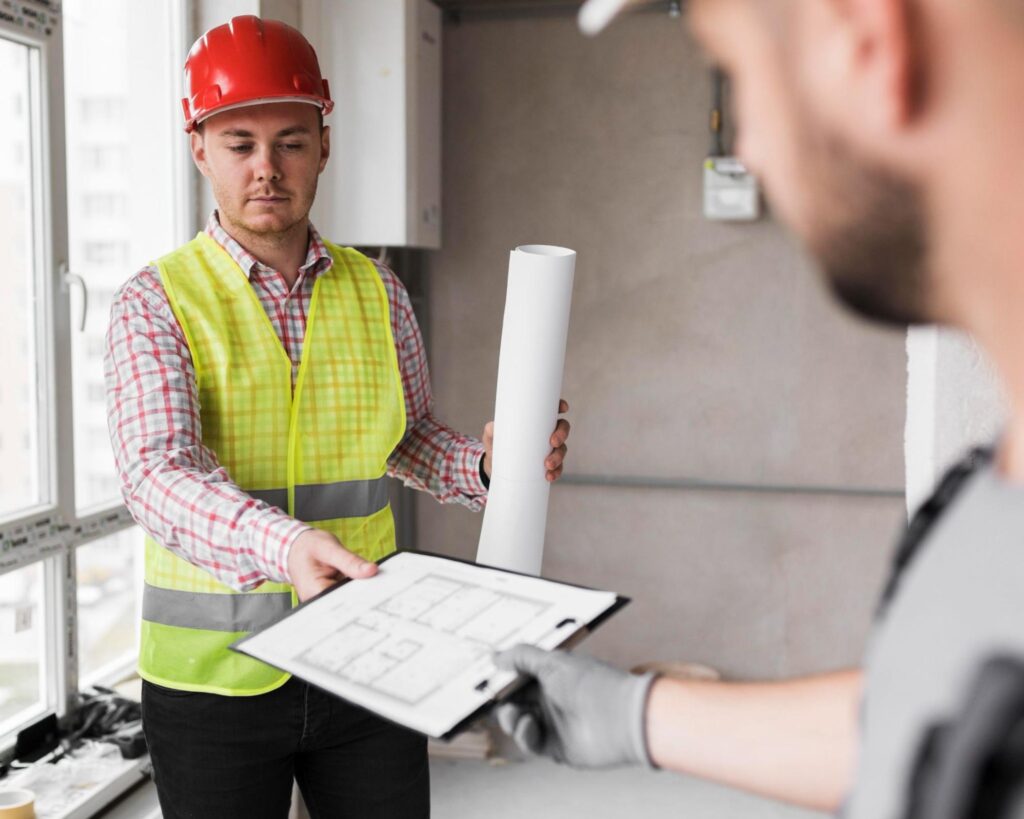Two workers completing a home inspection, one of them is handing a clipboard to the other who is dressed in a high-visibility vest and wearing a hard hat
