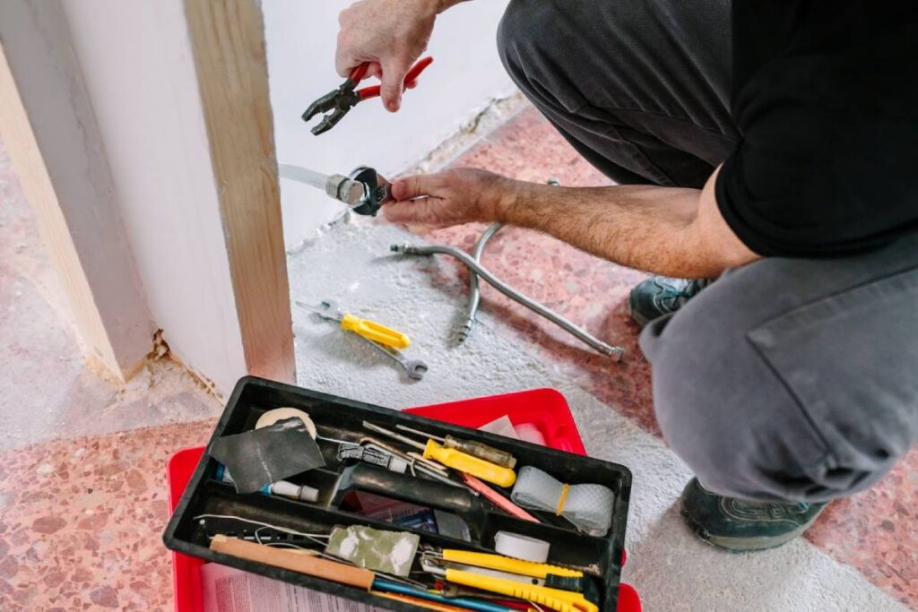 Person repairing plumbing pipes with tools and a toolbox during property maintenance.