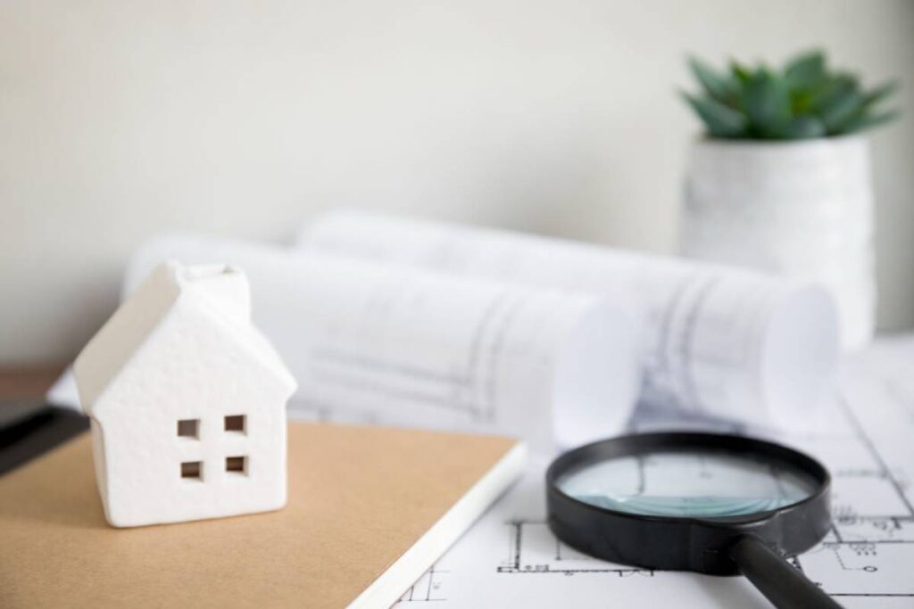 Small house model, magnifying glass, and building plans representing property inspections.