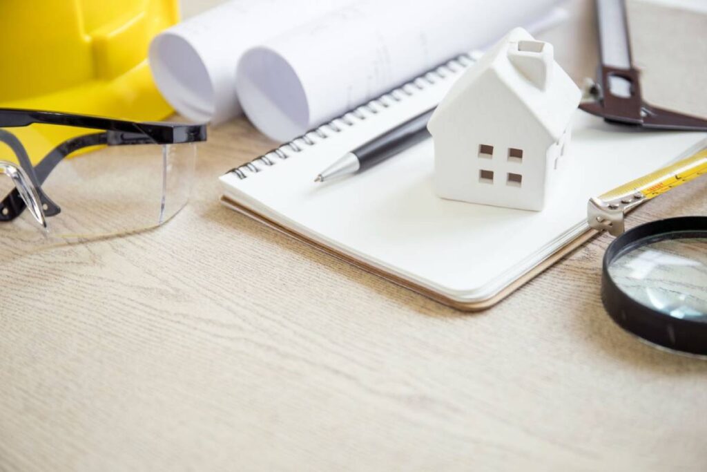 House model, magnifying glass, notebook, and safety equipment symbolising property maintenance and inspections.