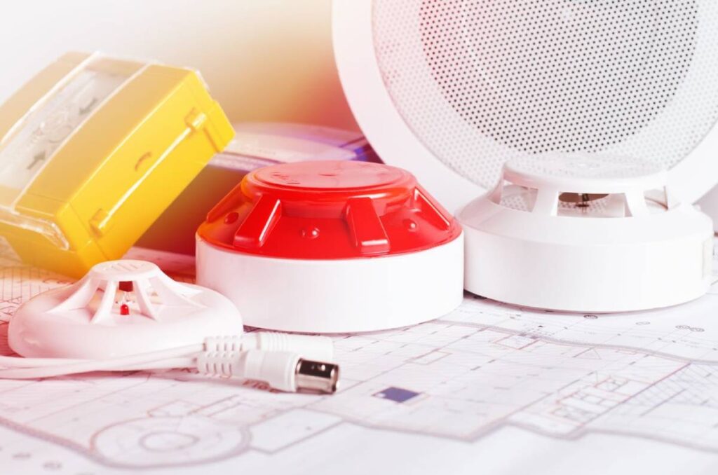 Various smoke detectors and safety devices are placed on house plans for property safety compliance.