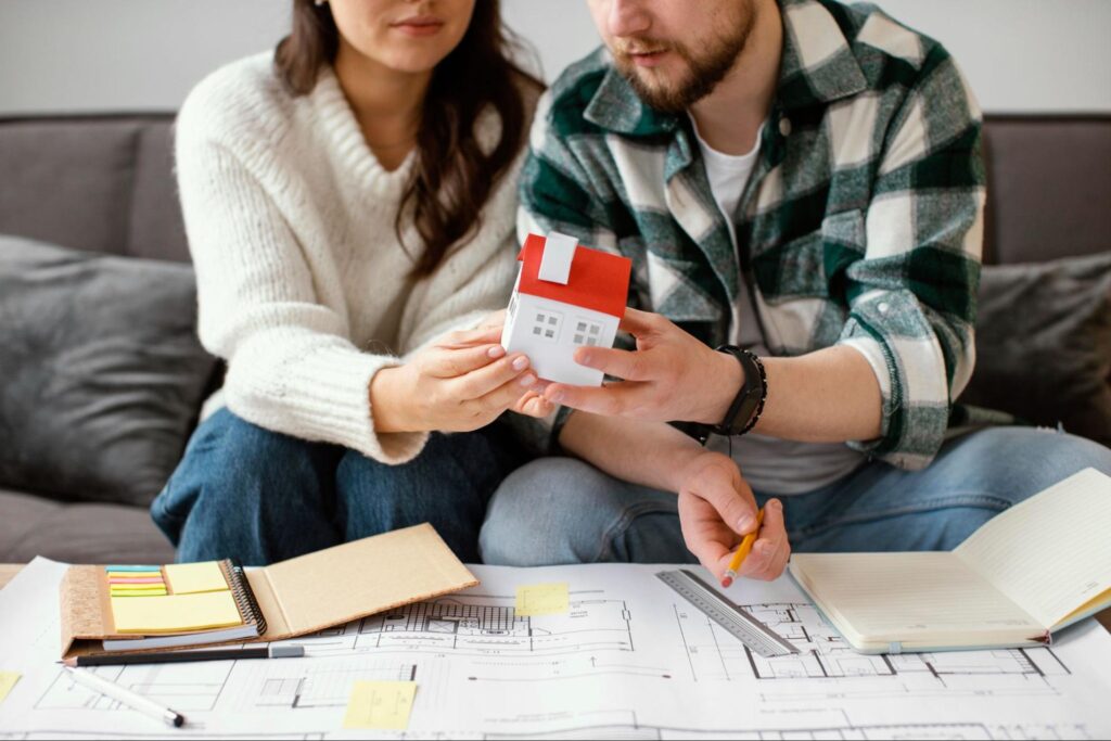 A couple looking over design plans and holding a small house structure.