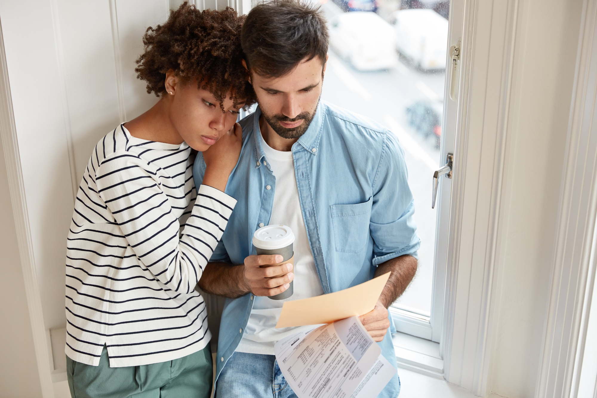 Couple sitting by a window reviewing rental property documents and inspection reports with a concerned expression.