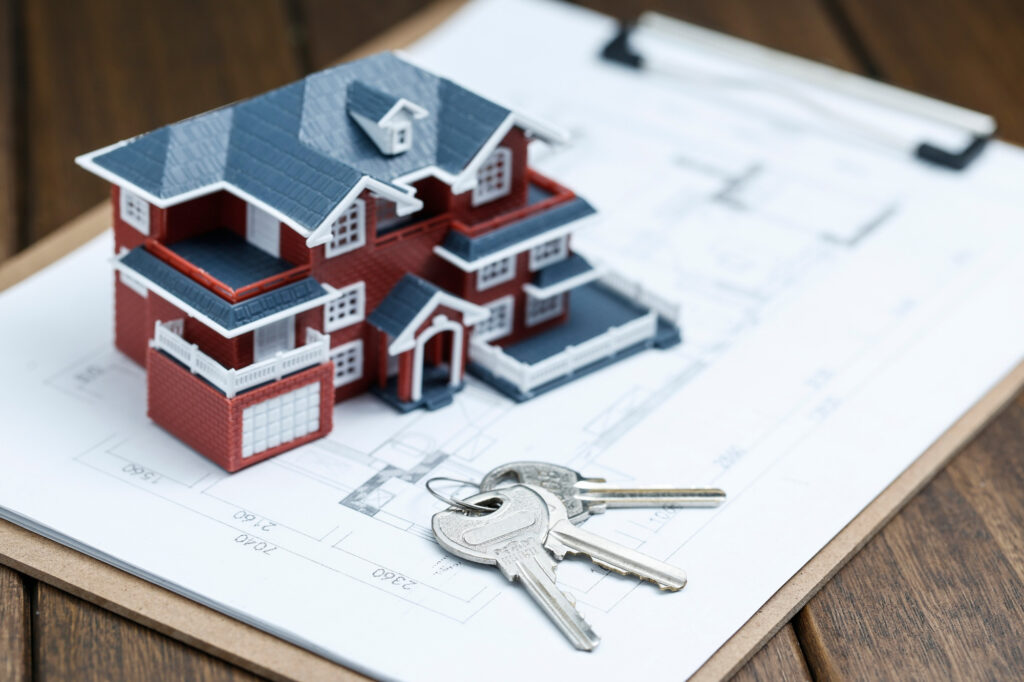 Model house sitting on architectural blueprints with a set of silver keys in the foreground, symbolising property ownership or home construction