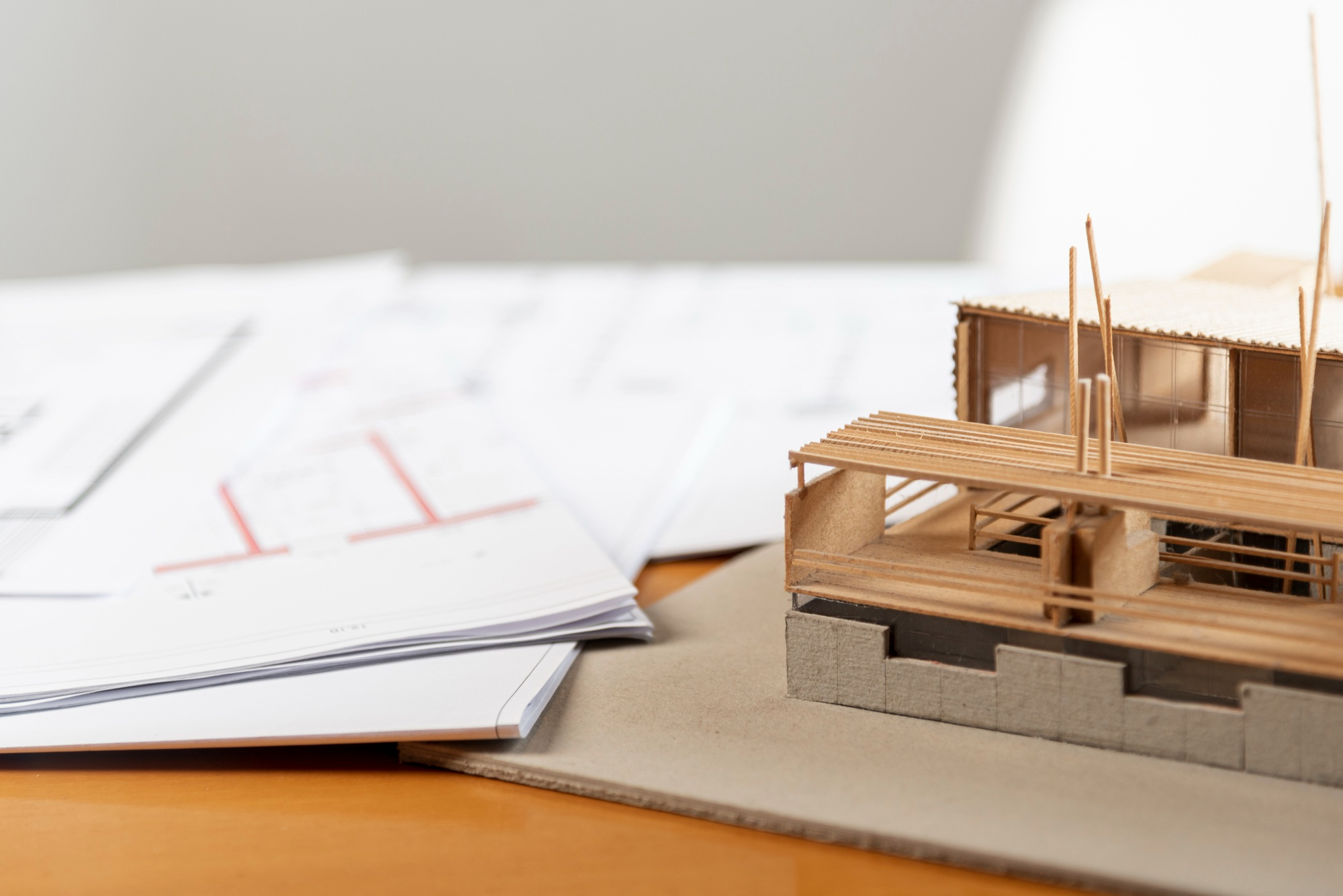 Miniature architectural model of a timber-frame building next to construction documents and design plans on a desk.