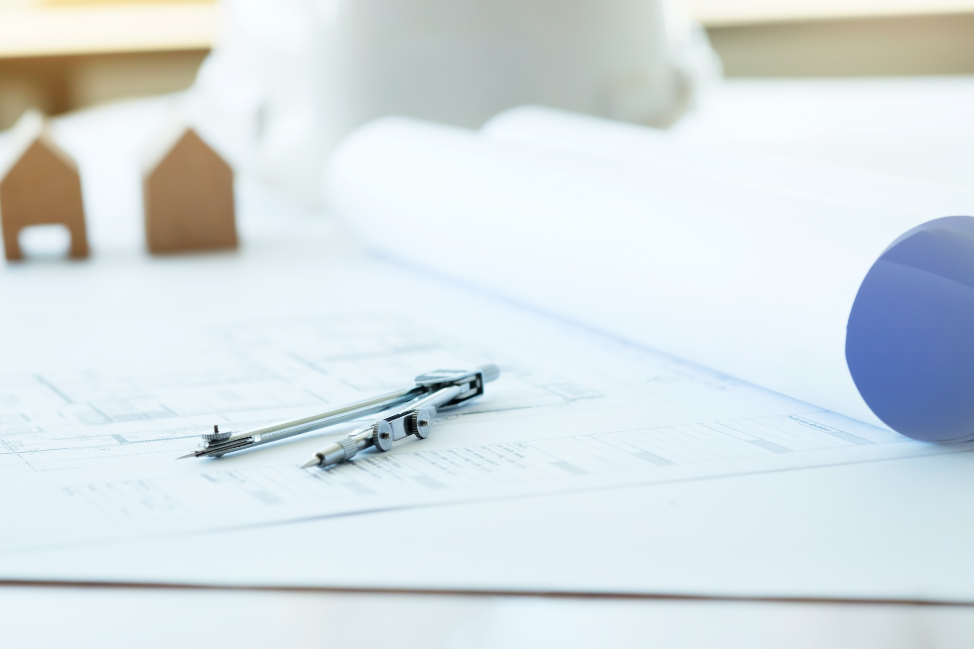 Close-up of rolled blueprints and a drafting compass placed on an architectural plan, suggesting technical drawing or design review.