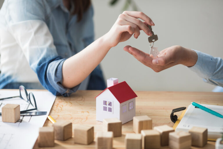 Close-up of house key handover with mini home model and paperwork, representing rental property transfer and landlord responsibilities.