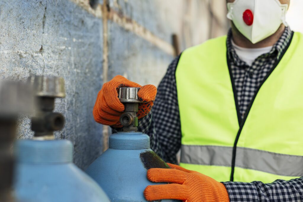 Technician in a hi-vis vest and gloves checking the valve on a blue gas cylinder during a gas safety inspection