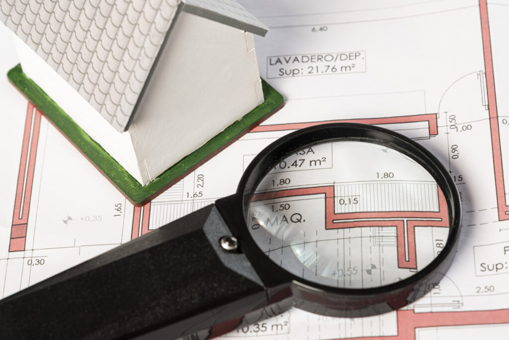 Model house and magnifying glass positioned over residential building plans during a property inspection review.