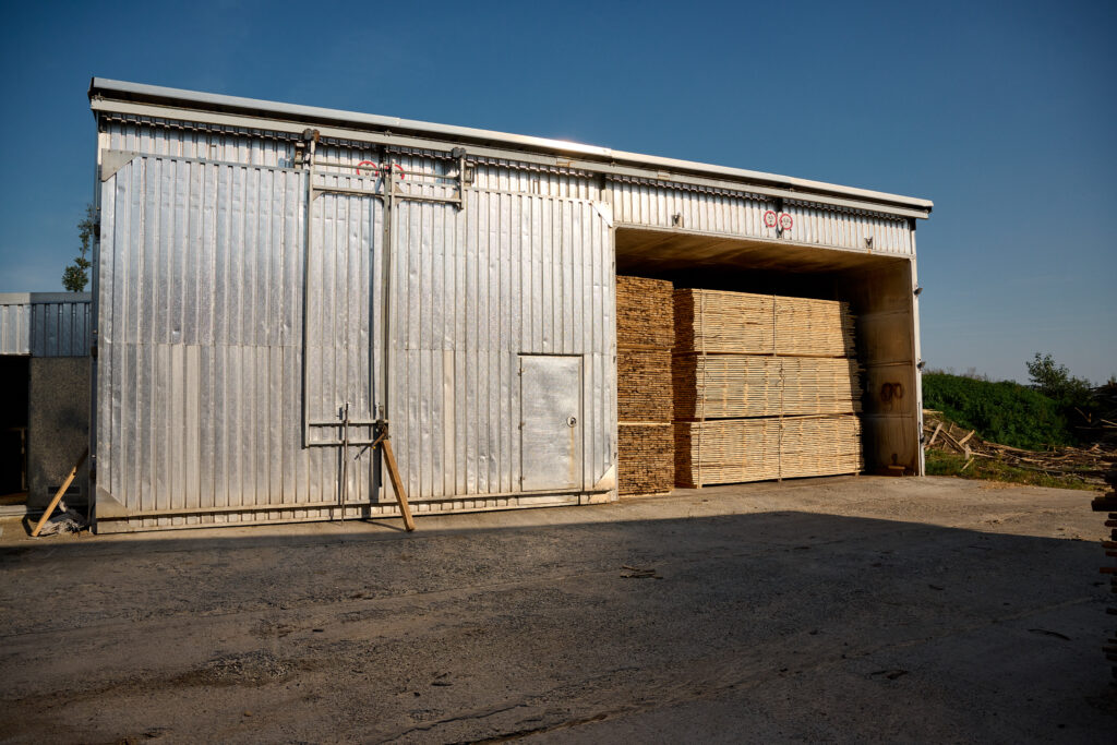 Large agricultural storage shed with corrugated metal walls and timber stacked inside the open bay.