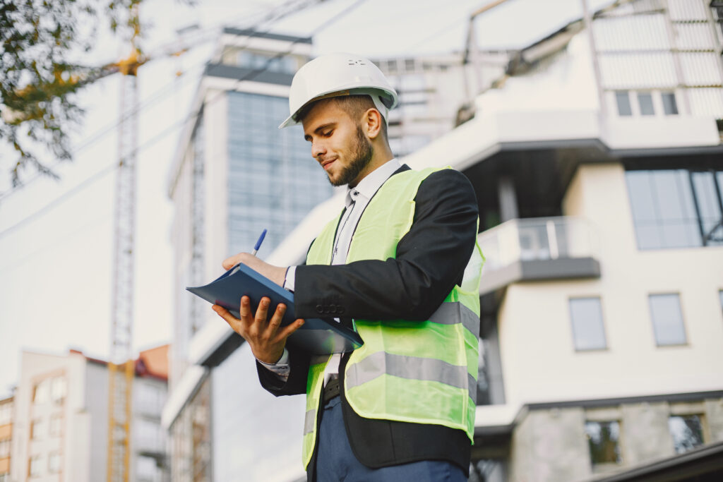 Construction professional wearing a hard hat and high-visibility vest taking notes at a building site.
