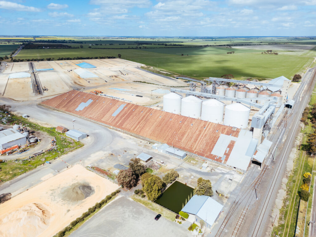 Aerial view of a rural Victorian property showing large agricultural storage buildings, grain silos, and surrounding flat farmland.