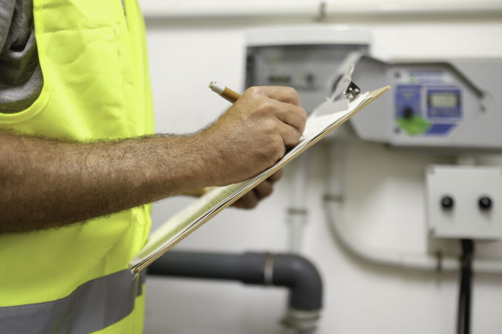 Inspector in a hi-vis vest writing up the safety check report on a clipboard