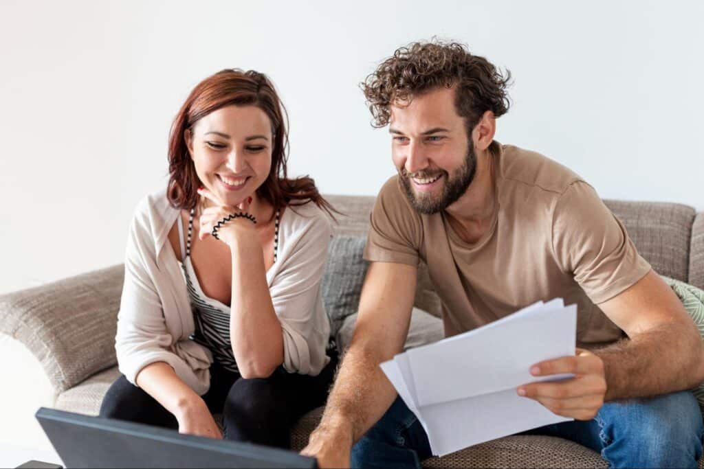 A happy couple smiling while checking the First Home Owner Grant on a laptop.